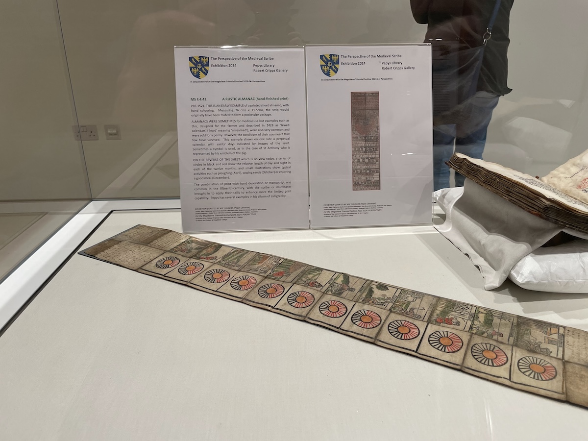 a folding printed almanac, displayed as an unfolded strip of paper segmented into months. Each month has a hand-coloured woodcut depiction of typical activities for that month, accompanied by a circle diagram using red and black lines to show the relative length of days and nights in that month. Accompanying display text gives some context to the object, and shows the reverse side of the almanac: a perpetual calendar, with saints’ days indicated by images of the saint.